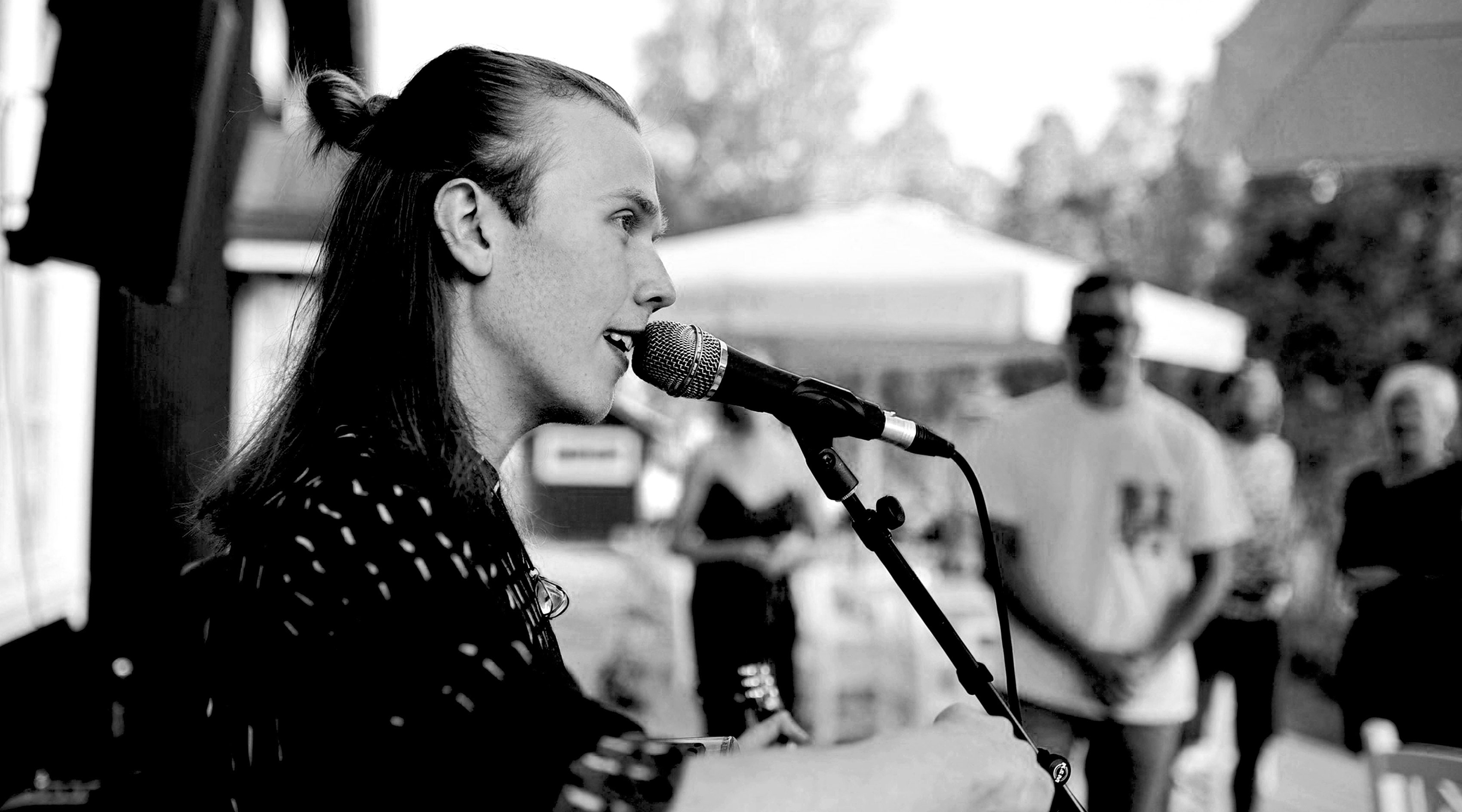 Erik Sjöholm singing into a microphone at an outdoor festival, audience behind